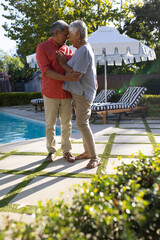 Obraz premium Elderly couple embracing by poolside, enjoying sunny day outdoors together