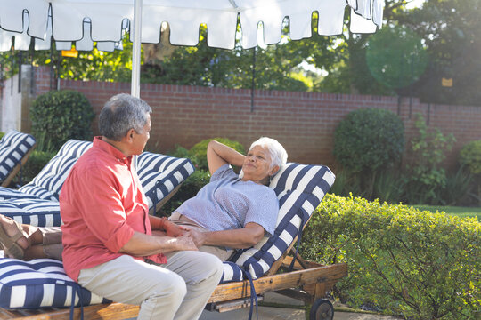 Senior couple relaxing on striped lounge chairs in sunny backyard garden