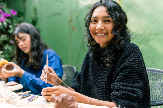 Two Latin American craftswomen working with clay in a pottery workshop, smiling while skillfully using tools to create beautiful ceramics
