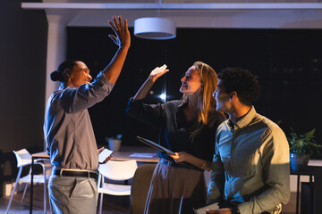 Fototapeta premium Colleagues celebrating success with high fives in modern office at night