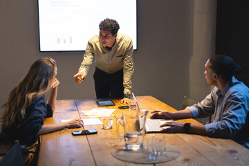 Fototapeta na wymiar Businessman presenting data to colleagues in conference room during evening meeting