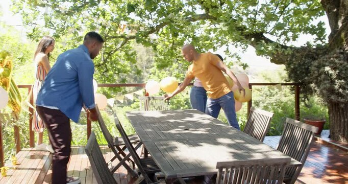 Group of happy multiracial and black male and female friends preparing table and decorations for bir