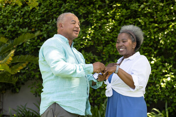Senior couple dancing joyfully in garden, enjoying sunny day together © wavebreak3