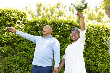 Senior couple celebrating outdoors, holding hands and raising bouquet joyfully
