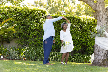 Senior couple dancing joyfully in garden, enjoying sunny day together © wavebreak3