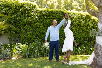 Senior couple dancing joyfully in garden, holding hands and smiling brightly © wavebreak3
