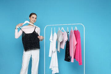 Smiling fashion stylist and rack with clothes on light blue background