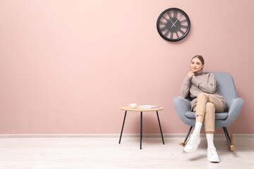 Beautiful woman relaxing in comfortable rocking chair near beige wall indoors, space for text