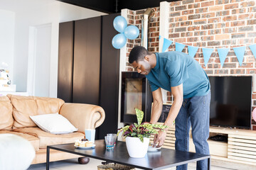 Mid adult African American man arranging potted plant on coffee table in living room, copy space