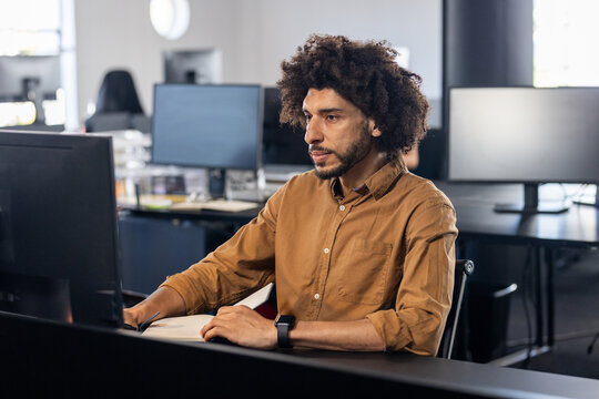 Young adult Asian man typing code at desk in open?plan office, with computer monitor and smartwatch - Powered by Adobe
