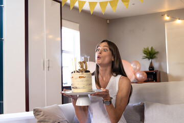 Woman holding birthday cake on stand with gold 30 topper, in room decorated with yellow bunting