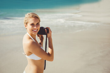 Female photographer is shooting beach scenes on sandy shore with DSLR camera near turquoise waves