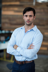 Standing male professional crossing arms in modern office interior, with wooden accent wall