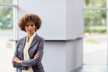 Standing African American woman crossing arms in office lobby, with glass windows