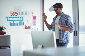 VR headset is resting on desk beside computer monitor in office, with colorful charts, copy space