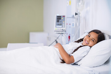 Smiling female child patient resting on pediatric ward bed with infusion pump tubing, copy space