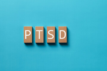 There is wood block with the word PTSD. It is an abbreviation for Post-Traumatic Stress Disorder as...