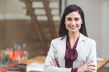 wooden desk holding colored pens and papers in office while ladder leaning against beige wall
