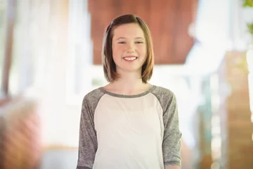 Fotobehang Teenage girl is standing in sunlit home interior near blurred window, showcasing gray-white shirt © WavebreakMediaMicro