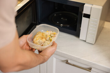 Man putting container with lunch into microwave in kitchen, closeup