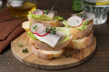 Tasty sandwiches with herring, radish and lettuce on wooden table, closeup