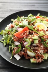 Delicious salad with brown rice on black wooden table, closeup
