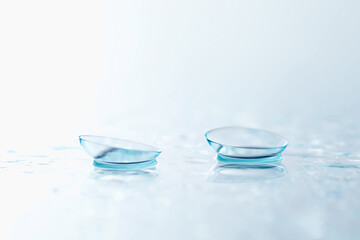 Pair of contact lenses and water drops on white mirror surface, closeup