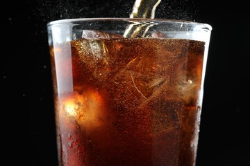 Pouring refreshing cola into glass on black background, closeup