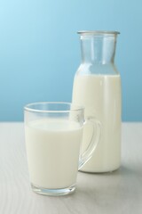 Fresh milk in cup and jug on white wooden table against light blue background