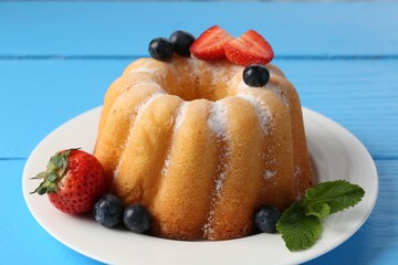 Tasty Bundt cake with powdered sugar and berries on light blue wooden table, closeup