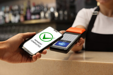 Payment terminal with NFC system. Client using mobile phone to pay for service in bar, closeup