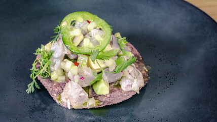 Fish mexican tostada with cilantro and jalapeno on dark plate