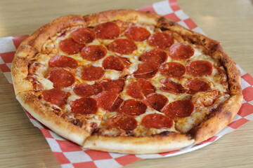 A mouthwatering classic pepperoni pizza sits on red and white checkered paper, showcasing golden crust and generous slices of savory pepperoni for an inviting food experience.