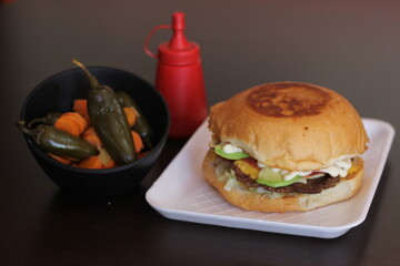 A scrumptious hamburger featuring a lightly toasted bun layered with fresh vegetables, pickles, and...