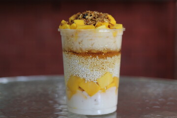 A vibrant mango yogurt parfait layered with creamy yogurt, fresh mango chunks, sweet syrup, and crunchy granola, perfect for a refreshing dessert or breakfast option.