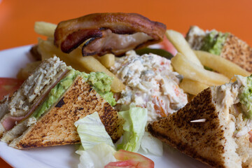 An appetizing chicken sandwich topped with creamy filling, crispy bacon, fresh vegetables, and served with golden fries, perfect for a filling lunch or dinner.