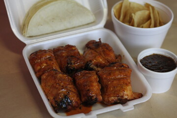A take-out box filled with spicy chicken thighs, accompanied by fresh tortillas and rich sauces, providing a cozy comfort food experience perfect for any casual gathering or meal.