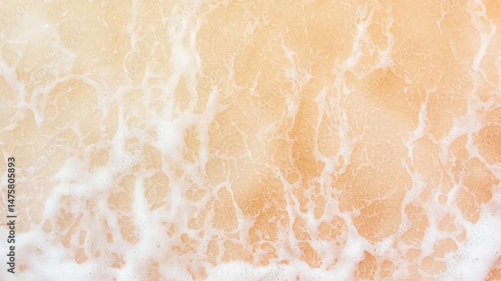Poster white sea foam spreads across a sandy beach, creating a delicate pattern with soft, warm lighting.