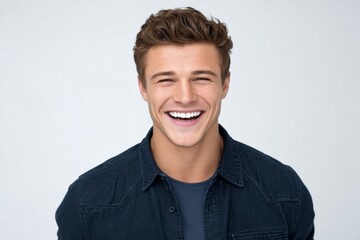 Young caucasian adult male smiling in casual denim shirt against light background
