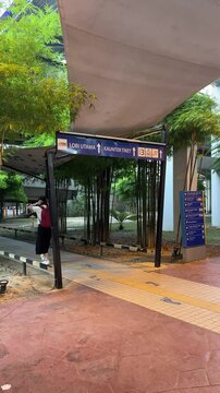 walkway leading to TBS Bus Station in Kuala Lumpur, with clear directional signs to the main lobby and ticket counter, surrounded by bamboo greenery and warm morning lighting