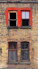 Fototapeta premium Rustic Brick Facade with Red Accents and Aged Windows Displays Urban Decay
