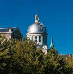 The iconic silver dome of Bonsecours Market rises above the trees in Old Montreal, Quebec. Captured on a clear blue sky day, this landmark reflects classic architecture and history.
