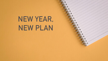New year, new plan. On yellow surface with open note pad. Top view.