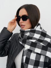 Fashionable woman in stylish sunglasses and plaid scarf poses against a neutral background