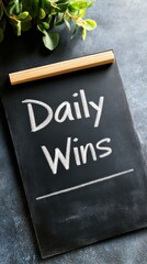 A motivational chalkboard with 'Daily Wins' written on it, surrounded by greenery, perfect for inspiring positivity and reflection.