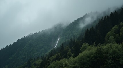 Obraz premium Serene Mountainscape with Waterfall and Foggy Atmosphere in Mysterious Forested Terrain