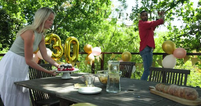 Happy black man and his white female partner celebrating thirtieth birthday in garden decorated with