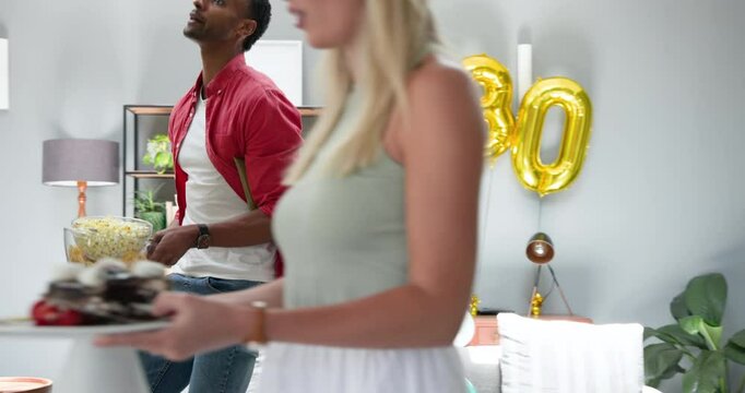 Happy black man and his white female partner cleaning room decorated with balloons after a house par