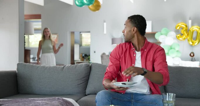 Happy black man and his white female partner cleaning room decorated with balloons after a house par