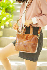 Brown leather shoulder bag and a girl in fashion clothes on an outdoor staircase background